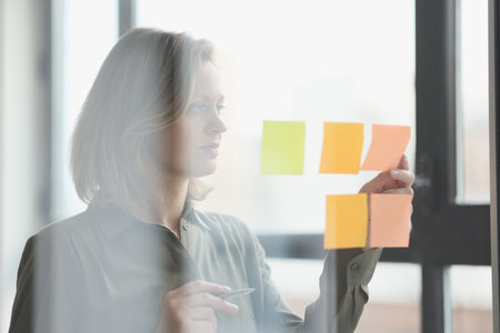 Female manager sticks note papers to transparent glass wall in office.の写真素材