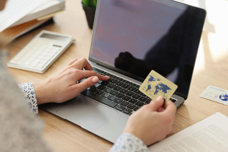 Woman with laptop computer holds credit card in her hand.