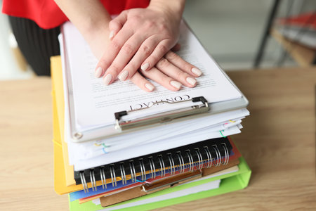 Female manager puts her hands on stack of office document, notebooks and clipboard.