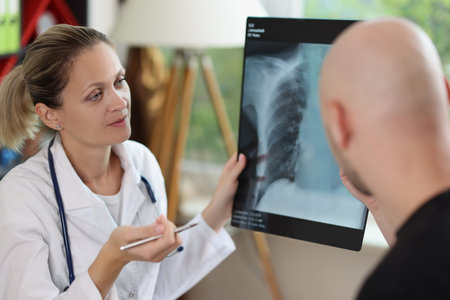 Female doctor holding x-ray image and pen in hands and speaking with male patient.の写真素材
