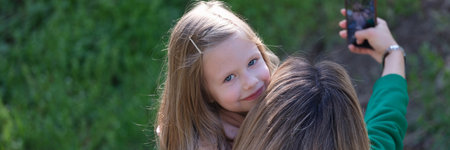 Mom and smiling daughter taking selfie on modern smartphoneの写真素材