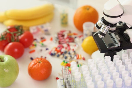Fresh fruits surrounded by scattered pills near microscopeの写真素材