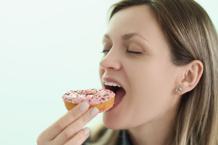 Happy woman bites delicious donut on light backgroundの写真素材