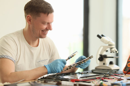 Smiling man studies broken motherboard in repair workshopの写真素材
