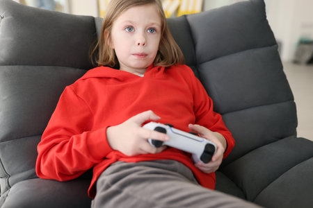 Focused teenage girl in red hoodie holds gaming consoleの写真素材