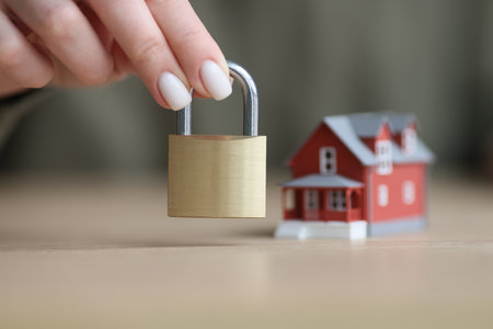 Hand of woman holding door lock near toy house model