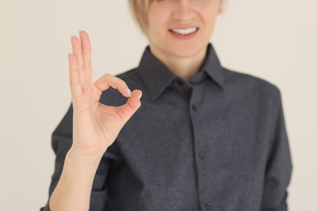 Woman shows OK gesture with hand smiling on beige backgroundの写真素材