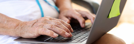 Elderly woman typing on laptop is looking for information on Internetの写真素材