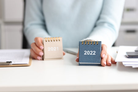 Woman holds calendar for 2021 and 2022 while sitting at deskの写真素材