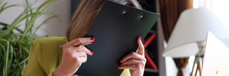 Overworked woman covering face with folder of documents