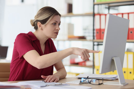 Suspicious woman points finger to screen of computer monitorの写真素材