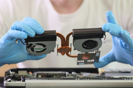 Master in rubber gloves holds cooling system of old laptop