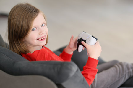 Cute little girl holds gaming console looking in cameraの写真素材