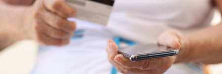 Old woman holding cellphone and bank card in hands