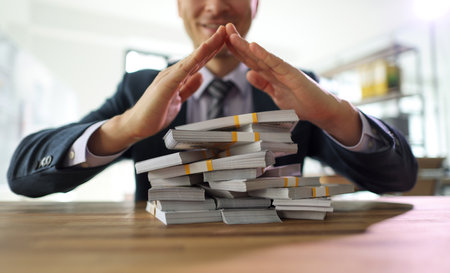 Businessman makes pyramid with hands above stacks of moneyの写真素材