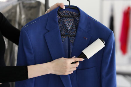 Woman removes pellets from blue woolen coat with rollerの写真素材