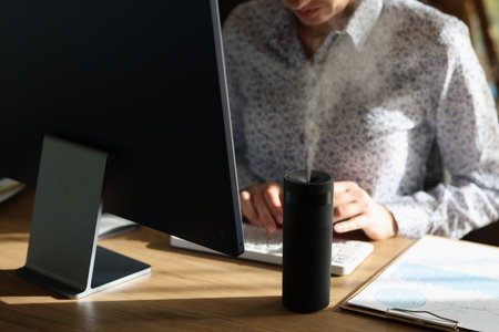 Woman types on keyboard while diffuser spreading aromaの写真素材
