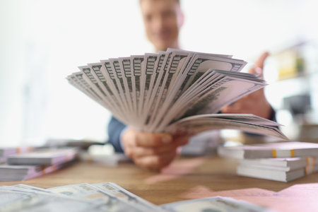 Man holds money fan in hands sitting at table with banknotes