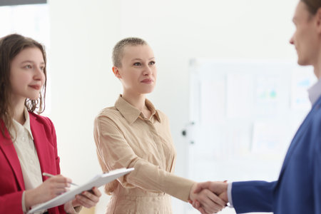 Happy manager watches colleagues shaking hands in officeの写真素材