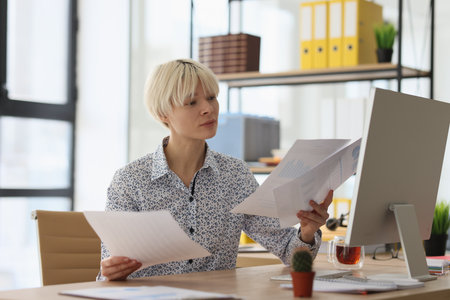 Curious blonde woman compares information reading papersの写真素材