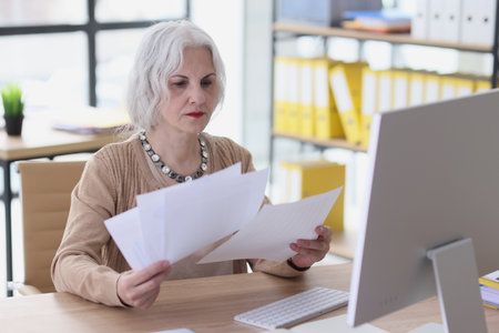 Thoughtful mature lady checks papers of agreement in officeの写真素材
