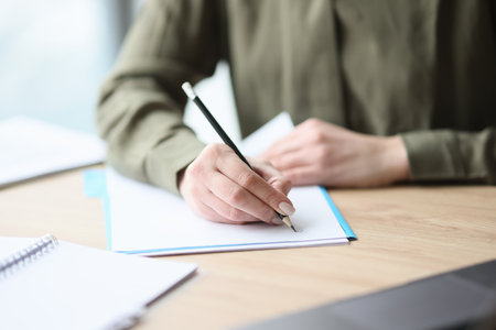 Woman writes on paper sheet with pencil sitting at deskの写真素材