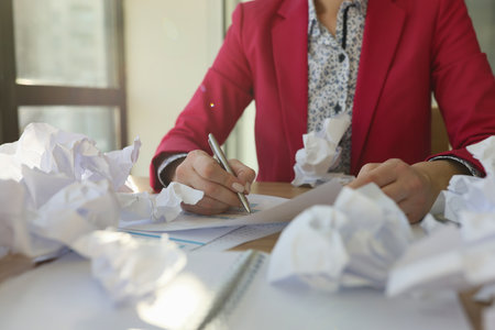 Woman writes reports at table covered with crumpled papersの写真素材