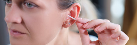 Closeup of young woman cleaning ear with cotton swabの写真素材