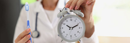 Female doctor stomatologist holding toothbrush and alarm clock in hands