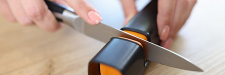 Woman sharpens knife with sharpener in kitchen close-up.の写真素材
