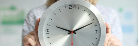 A woman in the office holds a wall clock, a close-upの写真素材