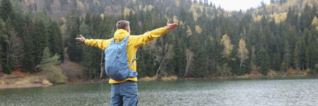 Man traveler with backpack standing at lake and mountains landscape