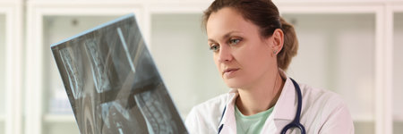 Female doctor examining x-ray scan film of patient while sitting at hospital.