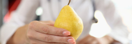 Close-up of pear in hand of nutritionist above medical office table.の写真素材