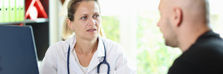 Female doctor listens attentively to patients story about his illness, sitting at hospital table.の写真素材