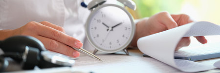Doctor with alarm clock and documents on hospital table.の写真素材