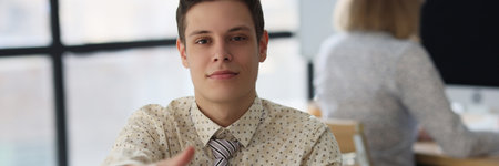 Male manager offers his hand for handshake while sitting at office desk.の写真素材