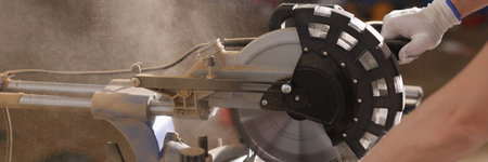Close up of working circular saw with hands of worker and dust in air.