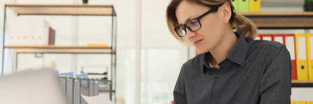 Focused female employee in glasses reads project papers
