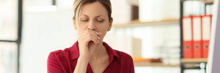 Female employee coughs sitting at desk at workplaceの写真素材