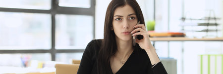 Concerned woman talks with manager on mobile phone in officeの写真素材
