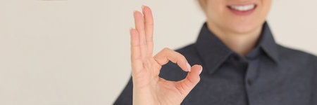 Cheerful woman shows OK symbol with hand smiling on beigeの写真素材