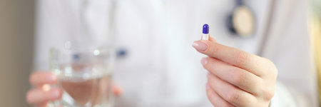 Female doctor holds vitamin pill and glass of water in handsの写真素材