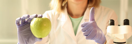 Woman holds green apple in hand showing thumb up gestureの写真素材