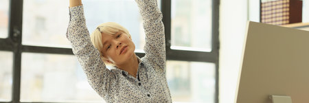 Overworked woman stretches arms and back sitting at table