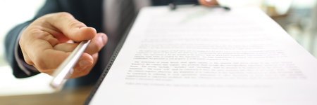 Manager gives contract papers and pen to partner in officeの写真素材