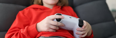 Focused schoolgirl plays video game sitting in armchair