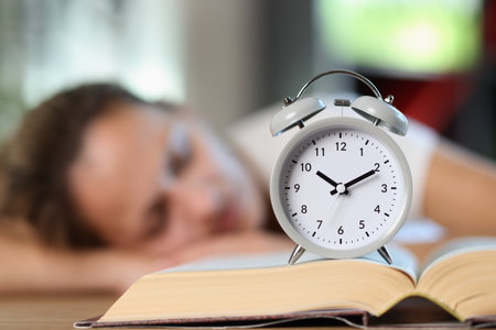 Overworked woman with book and alarm clock sleeps on office desk.の写真素材