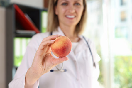 Smiling female nutritionist holds fresh peach fruit in her hand close-up.の写真素材