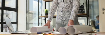 Designer standing near work desk with rolls of paperの写真素材